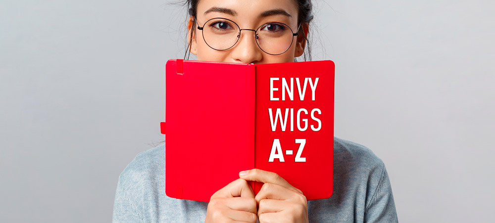 Woman in glasses holds up bright red notebook with “Envy Wigs A-Z” on the cover