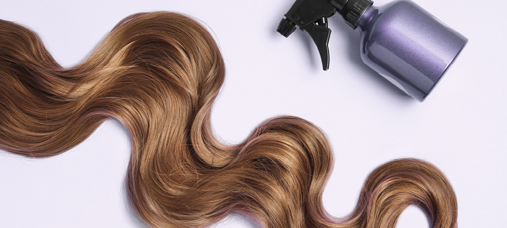 close up of a long, wavy lock of dark blonde hair and small gray spray bottle