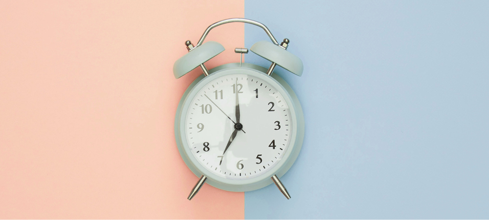 Old fashioned light blue alarm clock against pink and blue background