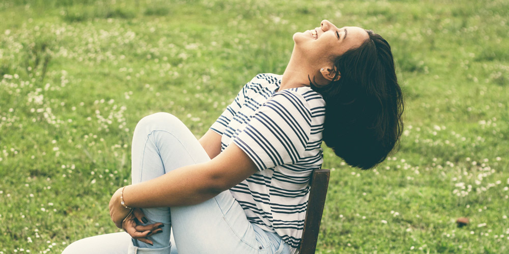 Woman reclines in chair on green lawn and smiles up at the sky